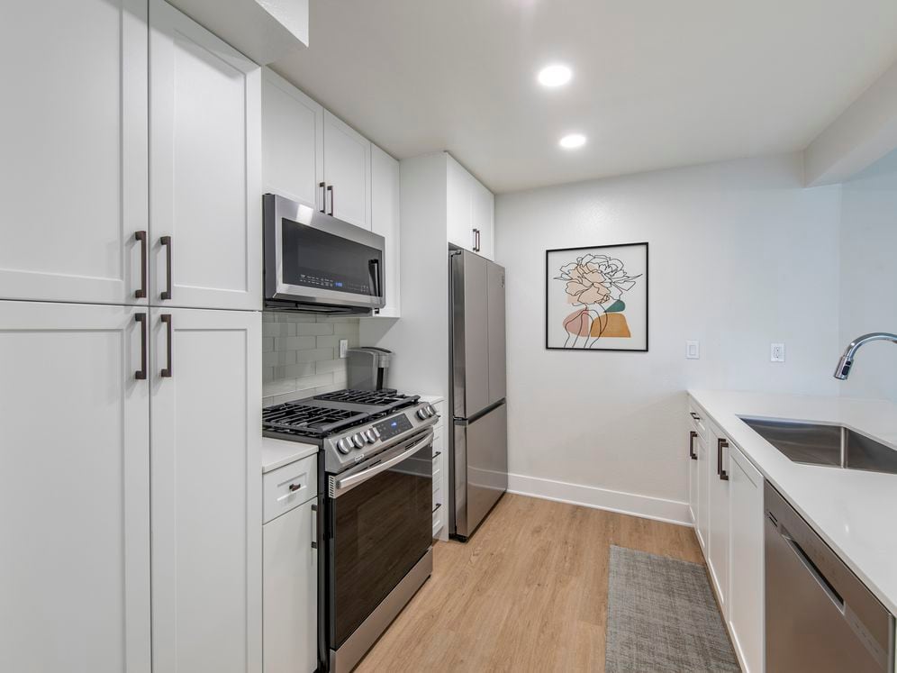 Renovated Package I kitchen with stainless steel appliances, white quartz countertops, white cabinetry, light grey tile backsplash, and hard surface flooring