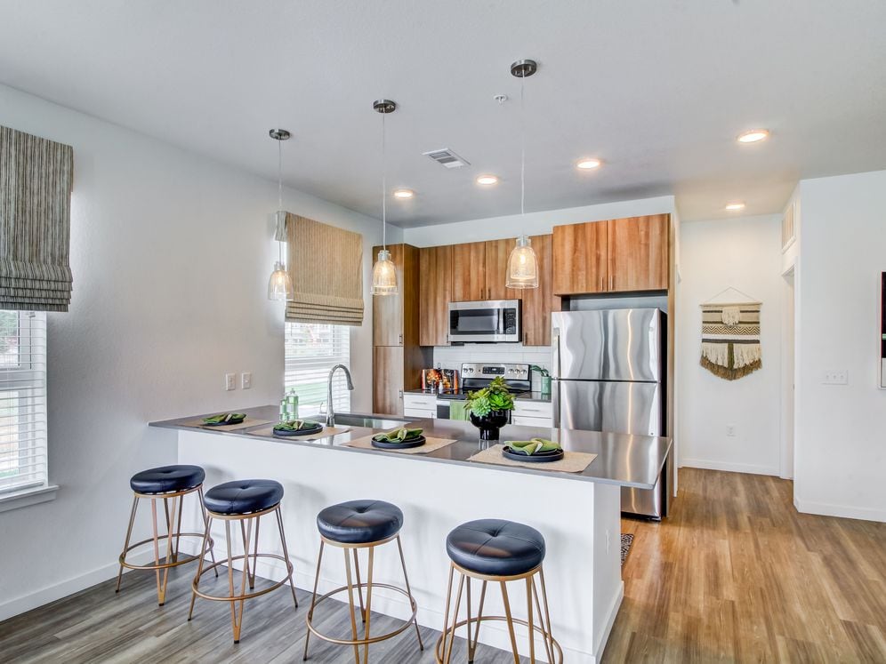 Kitchens feature oak upper and white lower cabinetry, grey quartz countertops, white subway tile backsplash, kitchen island or breakfast bar, and luxury vinyl plank flooring