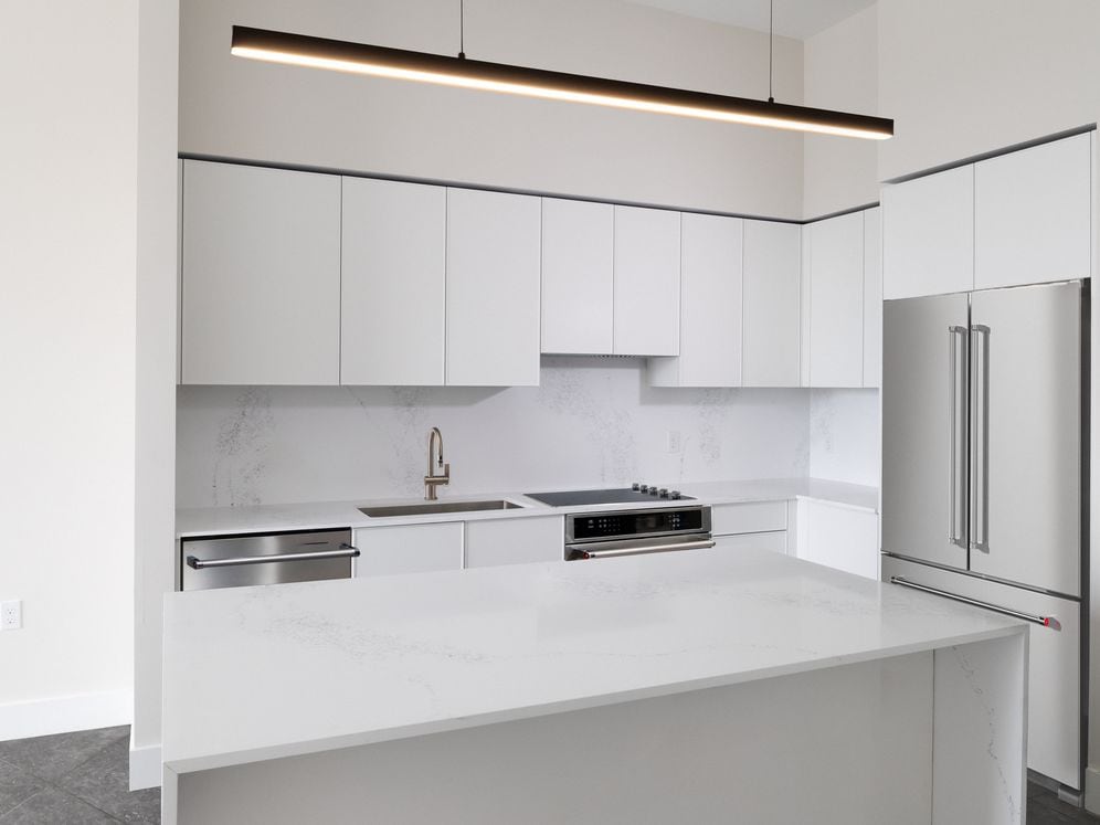 Signature Collection Three-bedroom apartment kitchen with white cabinetry, white marbled quartz countertop and backsplash, and upgraded stainless steel appliances