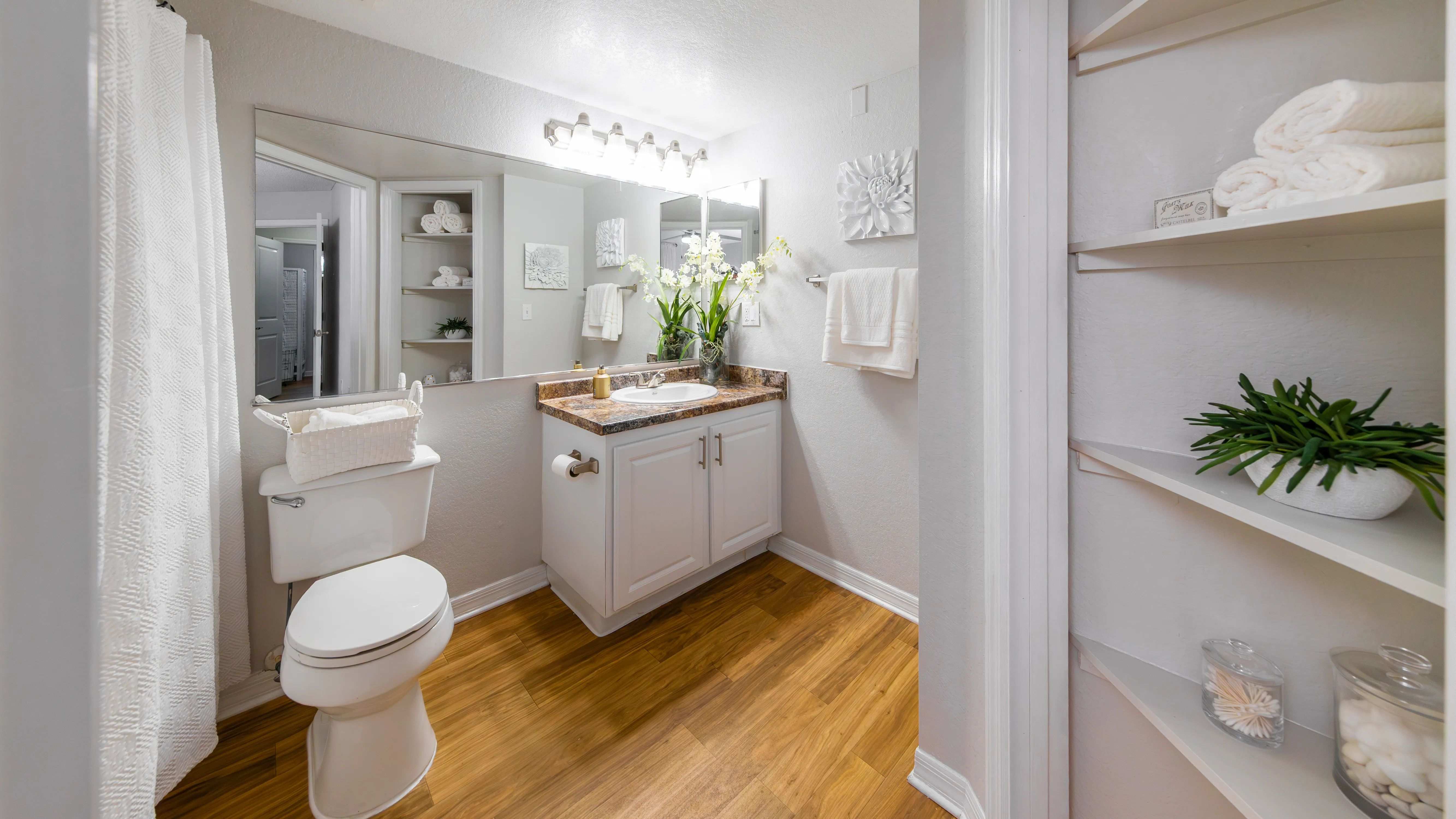 Our master bathrooms feature wood-style flooring, large mirrors, and a linen closet with built-in shelving.