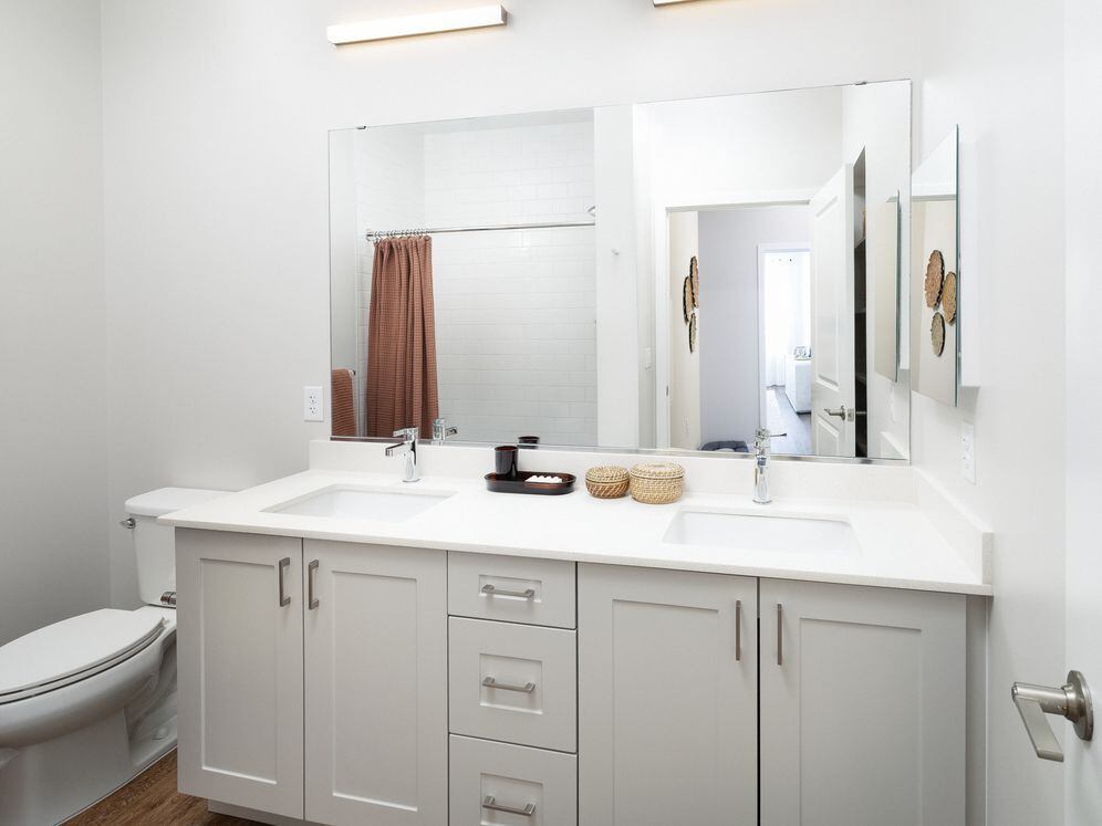 New West Phase apartments - Finish Package III Bathroom with white quartz countertops, grey cabinetry, and hard surface flooring
