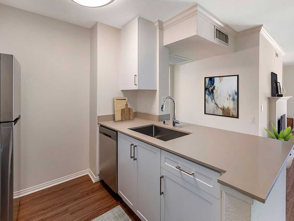 Renovated Package I kitchen with stainless steel appliances, beige quartz countertops, new white cabinetry, and hard surface flooring