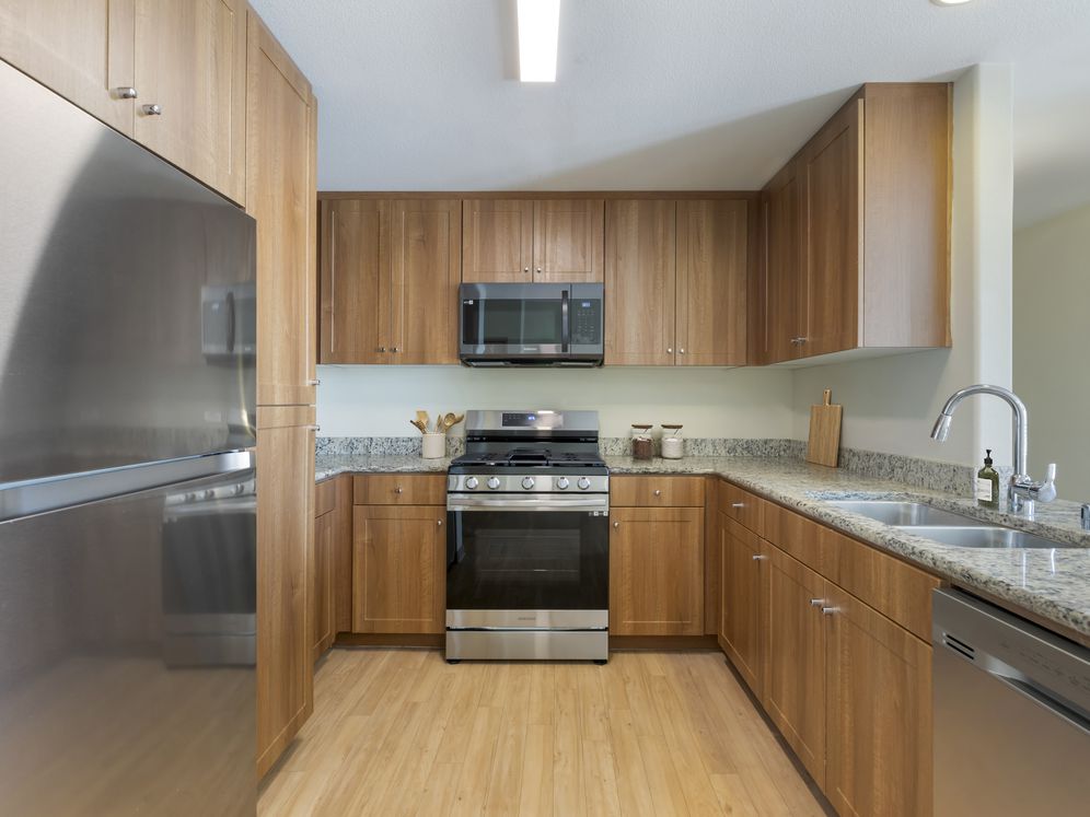 Updated Finishes kitchen with oak cabinetry, beige speckled granite countertops, stainless steel appliances, and hard surface flooring