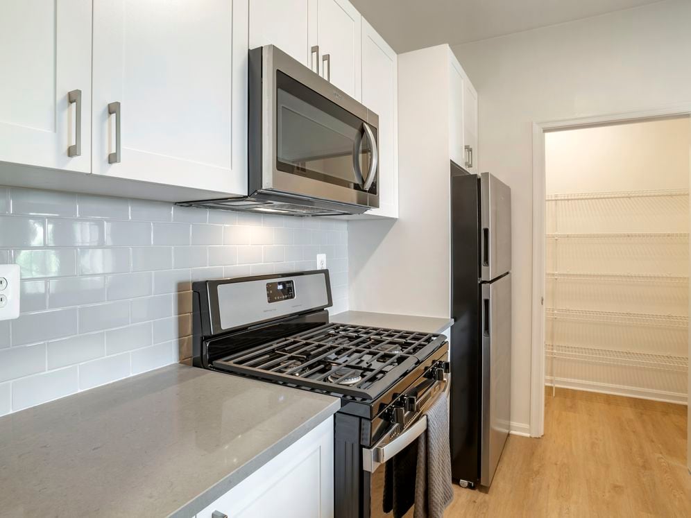 Renovated Package II kitchen with white cabinetry, grey quartz countertops, tile backsplash, stainless steel appliances, and hard surface flooring